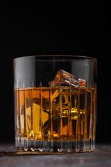 Single malt scotch whiskey in crystal glass with ice cubes on wooden background