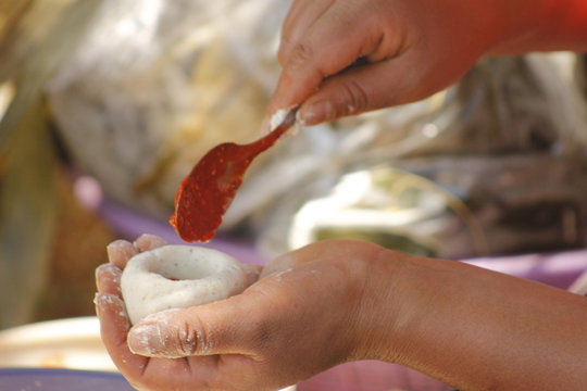 
hands of indigenous woman adding red sauce to make Mexican tamales called corundas
