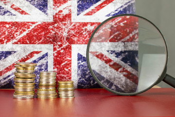 Magnifying glass and coins in front of United Kingdom flag, country economy concept