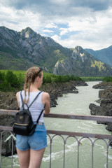 Fototapeta na wymiar Young woman standing on a bridge over a mountain river. Wonderful mountain landscape. Long distance travel. Happiness alone with nature.