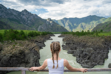 Young woman standing on a bridge over a mountain river. Wonderful mountain landscape. Long distance travel. Happiness alone with nature.
