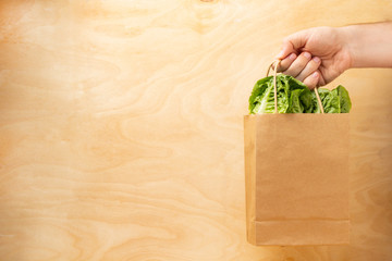 Hand holding mix of fresh salad in eco package on a wooden background.Food delivery.Healthy eating.