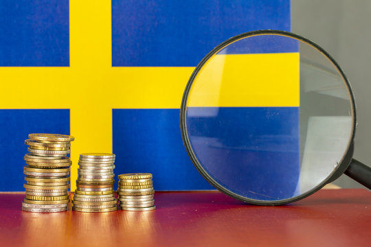 Magnifying glass and coins in front of Sweden flag, country economy concept	