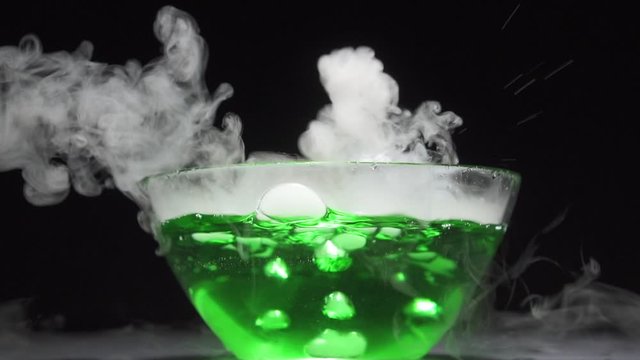 Magic potion is brewed in a glass bowl on a black background. Close-up, slow motion.