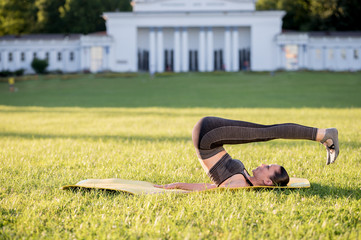 Fototapeta premium Beautiful young woman lying on a yellow mattress doing pilates or yoga, rolling back intermediate exercises