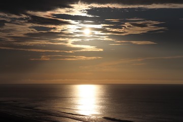 Dark twilight sky with gold and black clouds hiding the sun over a smooth glistening ocean