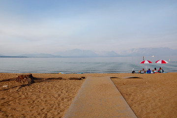 Bright Colored Beach Umbrellas Under Smokey Skies Over Lake Tahoe and Surrounding Western Sierras...