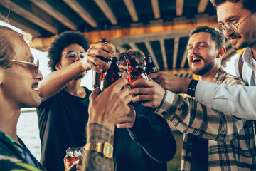 Group of friends celebrating, resting, having fun and party in summer day. Young men drinking beer, talking, laughting. Look happy and cheerful. Festive time, holiday, summertime, unity and friendship