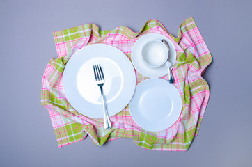 Kitchen towel, white empty dishes plates, cup on gray background, top view