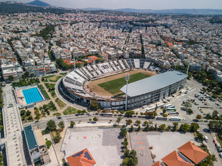 Thessaloniki, Greece landscape drone shot of PAOK FC Toumba stadium. Aerial top day view of empty football court with green pitch and team name written on the stands. - obrazy, fototapety, plakaty