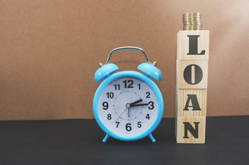 The word LOAN is written on wooden cubes. Business concept.Blue alarm clock and a stack of coins.