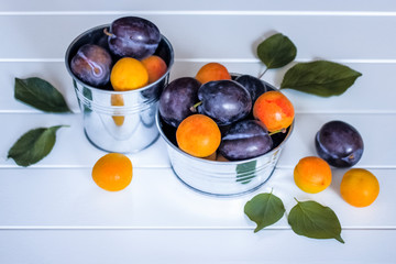 ripe plums and apricots close-up. background with plums and apricots. plums and apricots in metal bowls on a wooden background.