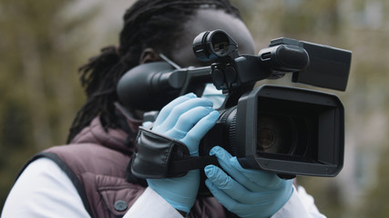 Young african man holding video camera with medical gloves. Reporting about covid19 spread. High quality photo
