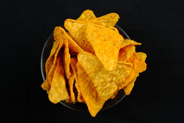 Corn chips on black background. A bowl of unhealthy junk food.