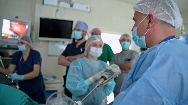 Surgery with modern medical equipment. Medical specialists in masks observe the surgical process on monitors. Medical team in operating room.