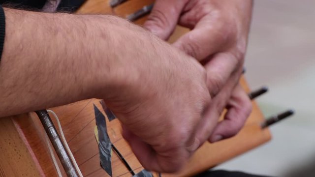 Close-up of a musician's hands playing the harp. A man holds a wooden folk instrument on his knees. The fingers strike the strings rhythmically.