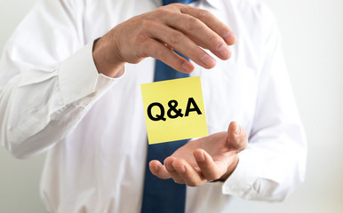 Q and A text word inscription acronym on yellow paperflying between male hands of businessman