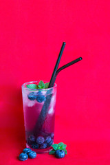 Blueberry juice with ice and mint. Cocktail with reusable iron tubes on a red background.