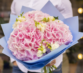 Young man holding a big bouquet of pink hydrangea and freesia in Women's day. Fresh bouquet flowers.