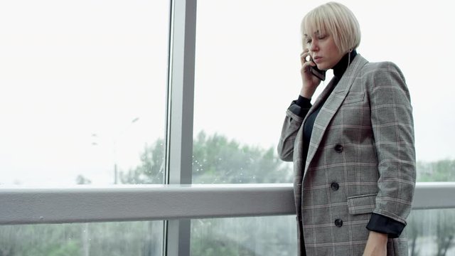 A side view slow motion close up shot of a blonde business woman being inside an office building and recieving a call from her business partner
