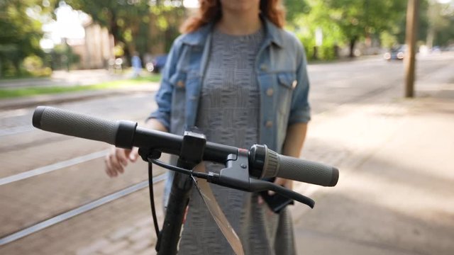 Happy bisexual woman rents electric scooter by phone app wearing rainbow LGBT bracelet
