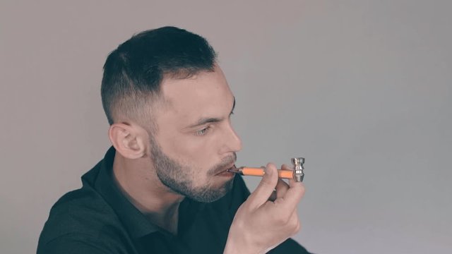 Young Man in Black Shirt Smoking Weed Indoors Using Pipe. Relaxation due to Ganja. Marijuana Culture Concept - Slow Motion. Close-Up View, Dynamic Shot
