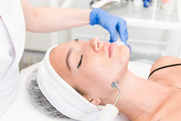 The young female client of cosmetic salon having microcurrent procedure on her face with special devices, close-up. Beautician using electrical impulses for facial procedures
