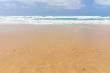 View of the ocean waves, sandy beach and sky.