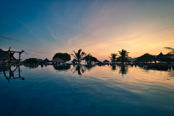 luxury swimmingpool on the beach during sunset with palms and reflections in the water. Lombok, Indonesia.