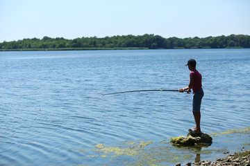 Silhouette of a boy standing on a rock and fishing with a fishing rod