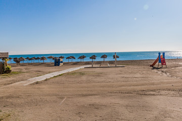 Empty beach with palapas on the shore and a game for children with the sea in the background, wonderful sunny and quiet day in Malaga Spain