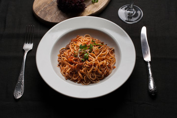 Spaghetti on a white plate on the background of a dark napkin with cutlery