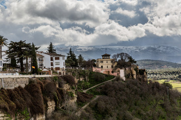 A part of the city of Ronda on a hill with its valley and snowy mountains in the background on a beautiful cloudy day with abundant white clouds in the province of Malaga Spain