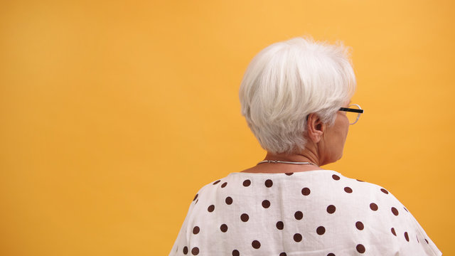 Back view of a senior woman isolated on the orange background. High quality photo