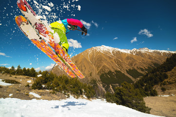 Girl skier in flight after jumping from a kicker in the spring against the backdrop of mountains and blue sky. Close-up wide angle. The concept of closing the ski season and skiing in spring