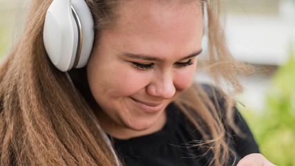 Close-up portrait of chubby woman wearing headphones and listening to music outdoors