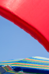 Close-up view of two open beach umbrellas, one red and one multi-colored