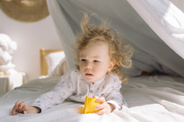 Fototapeta premium Little boy with curly blonde hair playing in bed. Sleep time concept.