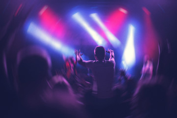 Hombre joven divirtiéndose en festival, en uno de los conciertos, con las dos manos arriba y luces rojas y azules de fondo - obrazy, fototapety, plakaty