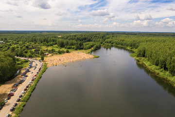 Beach with vacationers and a line of cars near the village of Khromtsovo on a sunny summer day.