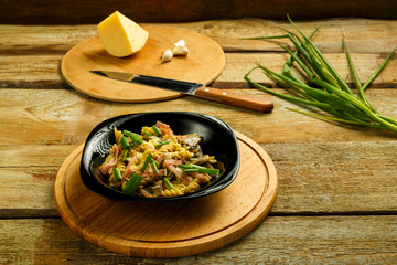 Black plate with pasta with ham and mushrooms in a creamy sauce on the table with a fork in the background.