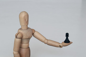Wooden figurine holds black pawn in his hand