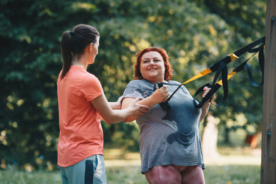 An obese woman together with her trainer during weight loss training, does arm and chest exercises