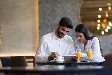 The couple is sitting at a table in a restaurant and drinking orange juice, looking at a notepad together, she talks