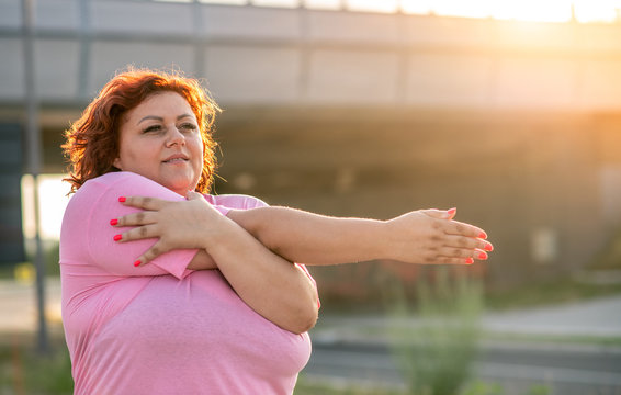 An obese woman does a warm-up exercise on a sunny day