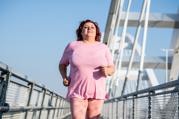 An obese woman jogs on a sunny day, doing extra weight training