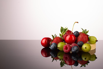 Summer berries on the table with reflection:strawberries,cherries,raspberries,goosberry and blueberry,with fresh mint leaves.