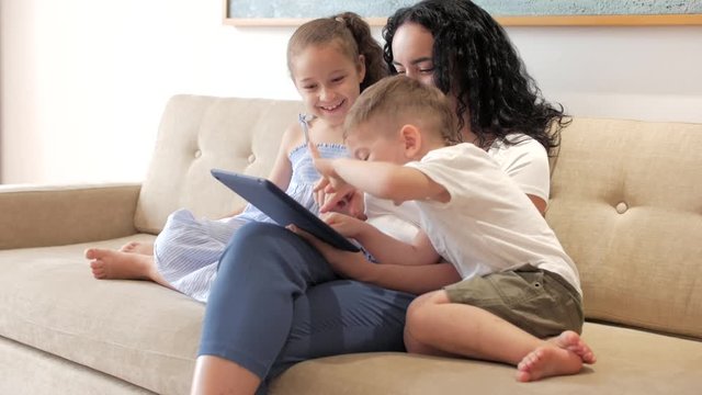 Happy family, mom and cute little children watch the phone, mom plays with children at home, relaxing using a smartphone, hugging, sitting on the couch, laughing, having fun, enjoying moments of