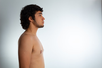 Obraz premium Young nude Hispanic man with wavy hair and shaved beard on a white background, expressing confidence