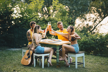 Two couples are sitting outside in nature, talking, enjoying and toasting with beer
